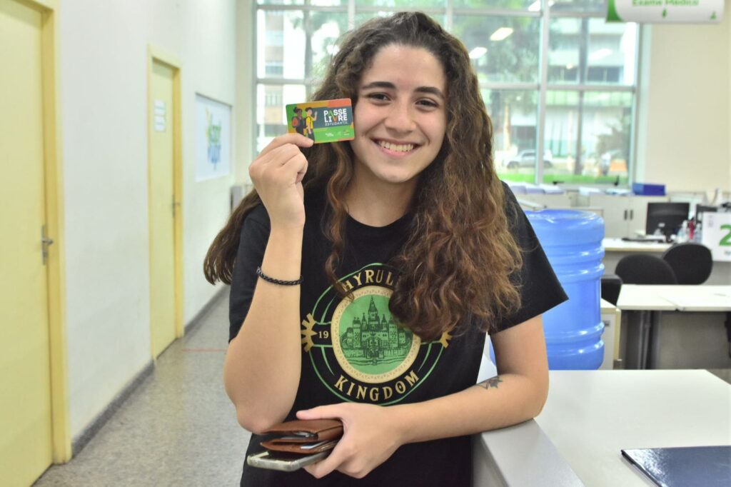 Uma garota branca vestindo camiseta preta e segurando o cartão do PLE