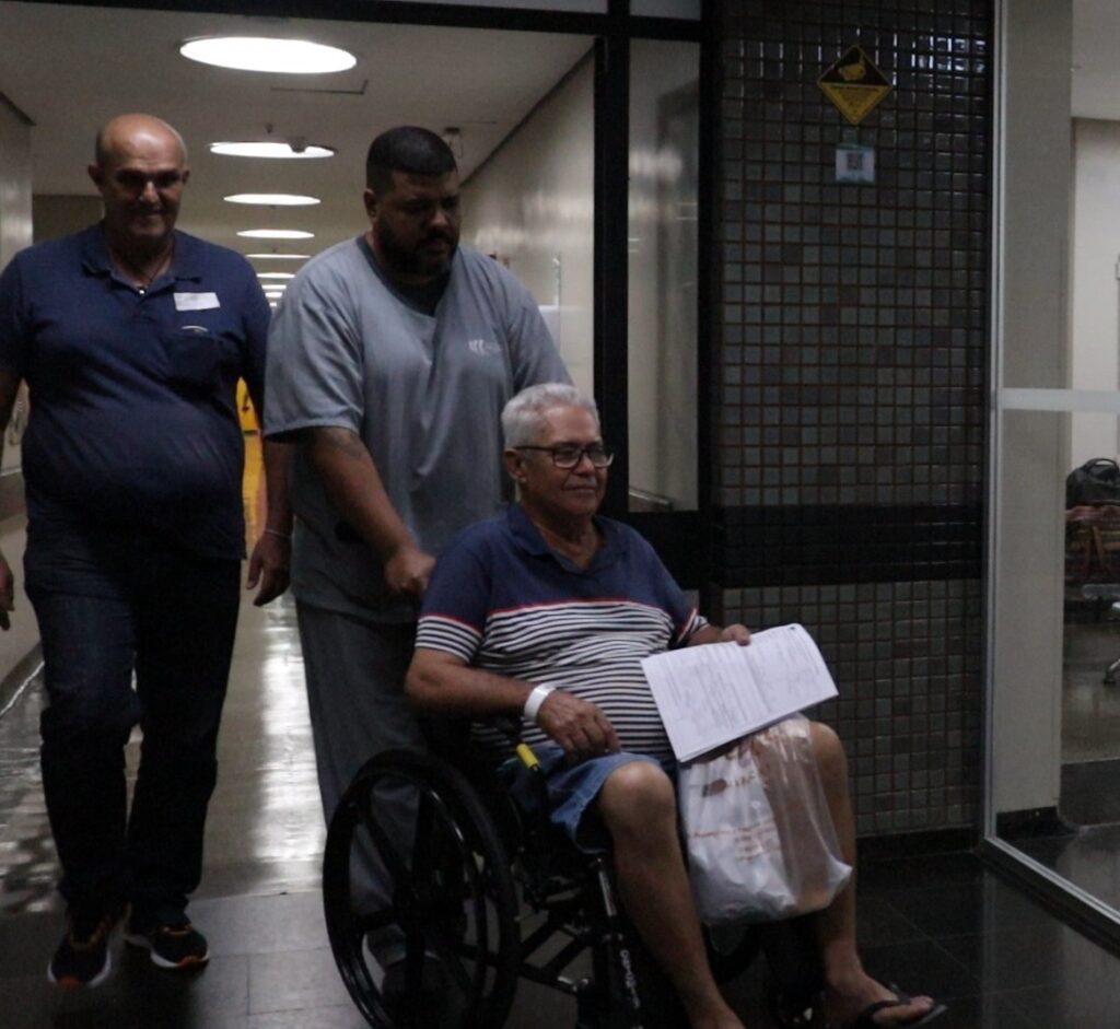 Paciente sendo transportado em cadeira de rodas no corredor do HGG