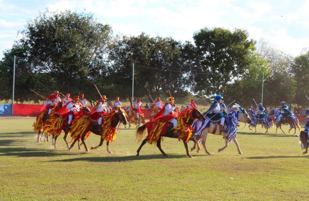 Governo de Goiás inclui Guarinos no Circuito das Cavalhadas em 2026 - Encenação da batalha entre mouros e cristãos com cavaleiros e animais em trajes nas cores vermelho e azul
