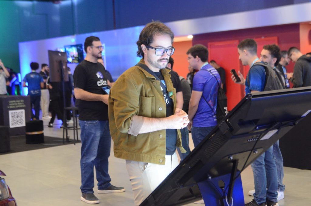 Goiás sedia um dos principais eventos do país voltados à inteligência artificial: Conecta Ceia – AI Brasil - homem jovem, branco e de pé diante de diante de tela de computador