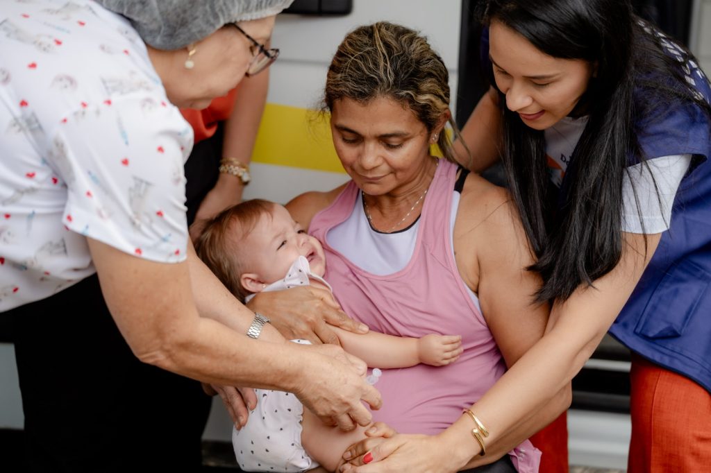 MÃE SEGURA CRIANÇA NO COLO PARA RECEBER VACINA CONTRA A GRIPE