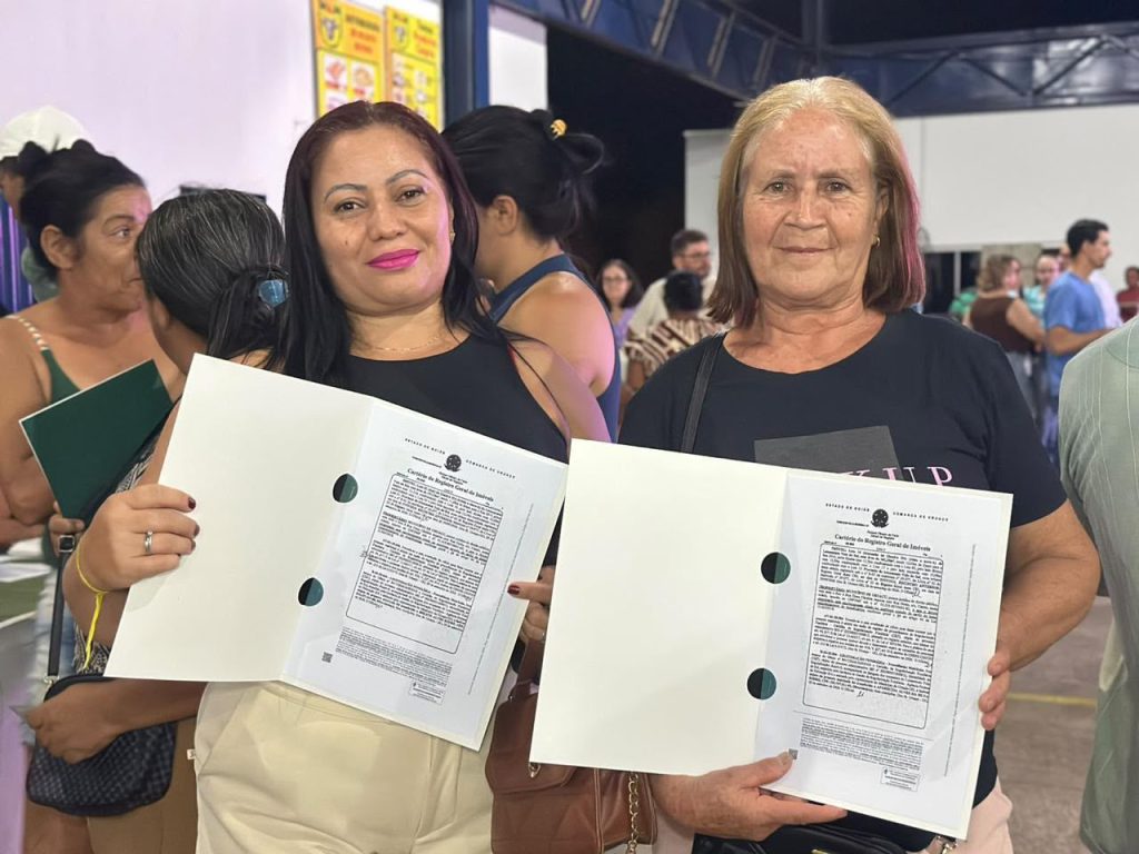 Agehab põe fim à espera de 70 anos por escritura em Acreúna - Duas senhoras vestindo preto e segurando escrituras de seus imóveis SEGURANDO ESTITURAS