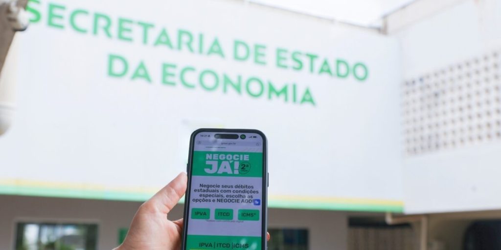 Governo de Goiás vai ampliar abrangência do Negocie Já II - achada da Secretaria de Economia ao fundo e em primeiro plano um celular com tela aberta na página dod programa